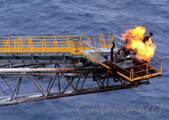 Aerial of multi outlet flare on the boom of an offshore platform-burning excess gas