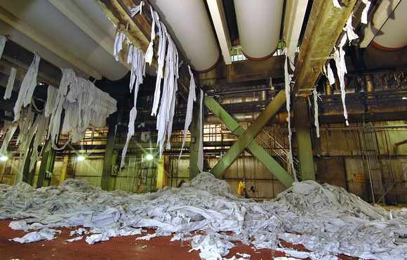 Manufacturing rolls of paper for newspaper print -seen from underneath the machinery where scrap shreds and rips build up