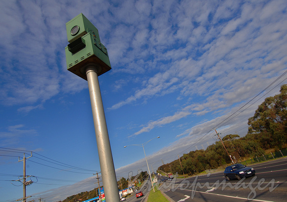 Speed camera mounted high on a pole stands on the centre medium strip major road Melbourne