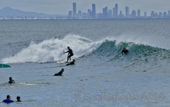surfers ride the waves at BUrleigh Queensland beach with a Surfers Paradise backdrop