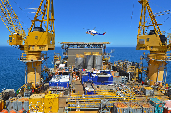 Offshore platform main deck activity with helicopter lifting off helipad