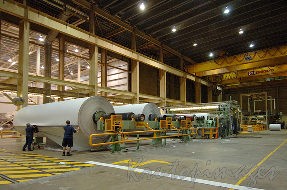 Paper manufacture workers setup huge rolls of newsprint prior to cutting into smaller rolls