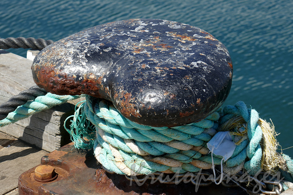 mooring ropes around an old mooring bollard-trapped in the coils is a facemask re covid