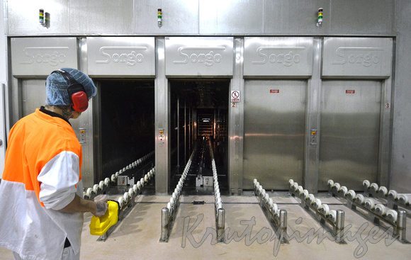 Industrial ovens cooking hams checked in transit by a worker with a torch