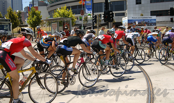 Female cyclists race around a roads track crossing tramlines in the Docklands Melbourne